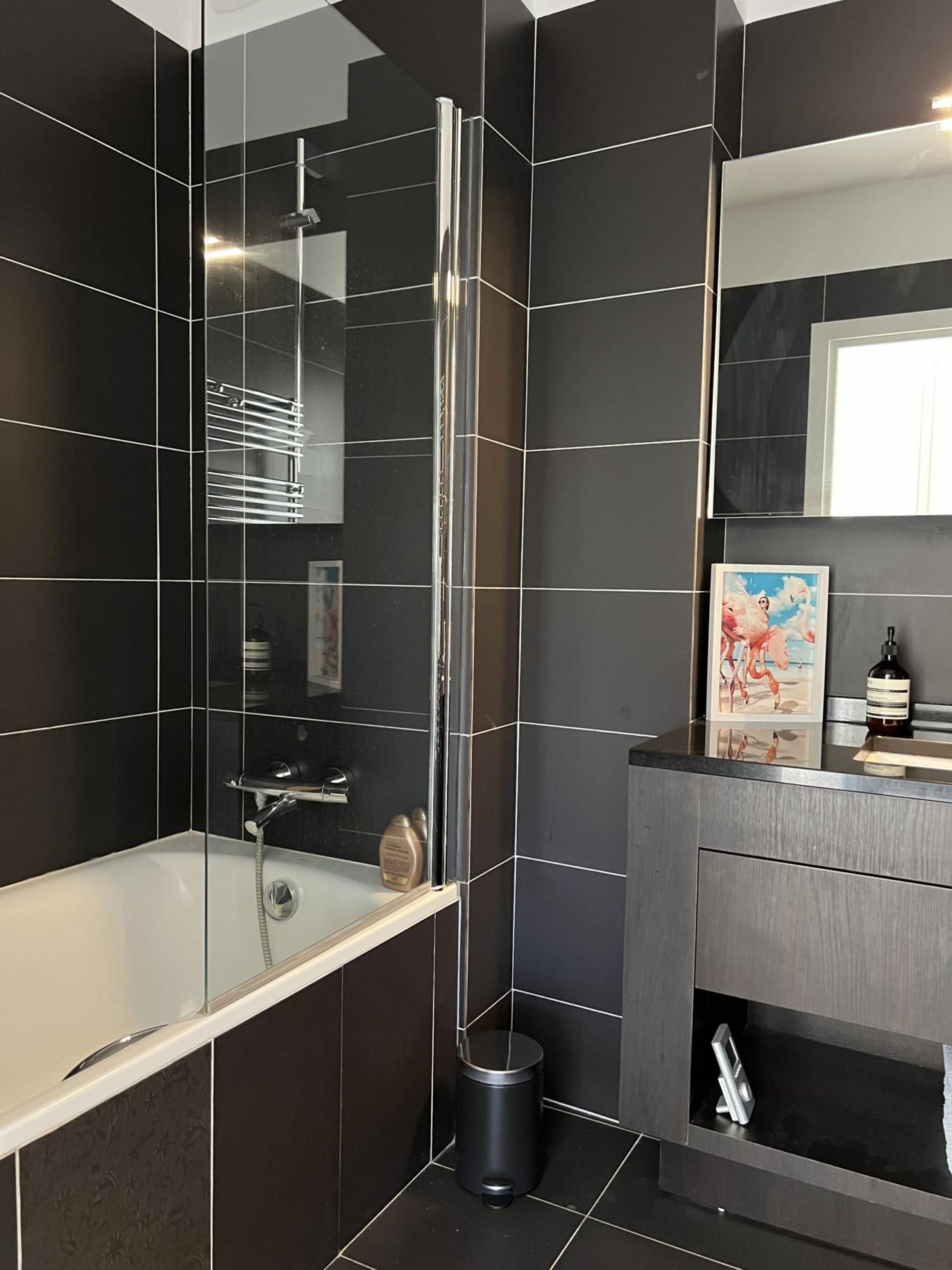 A modern bathroom with a glass-enclosed shower, a vanity with a mirror, and a trash can.