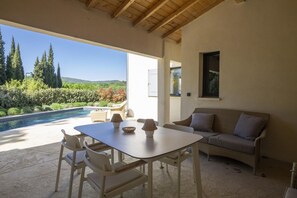 An outdoor patio with a table and chairs, a sofa, and a view of a swimming pool and greenery. - Villa Tica in Malauc ne (Malaucene)