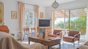 Un salon spacieux doté d’un grand téléviseur, de sièges confortables et offrant une vue sur la verdure environnante.