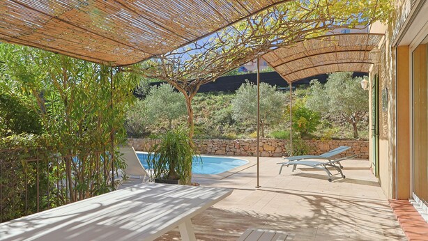 Un espace extérieur aménagé en terrasse, avec une piscine, des chaises longues et une table placée sous une pergola ombragée.