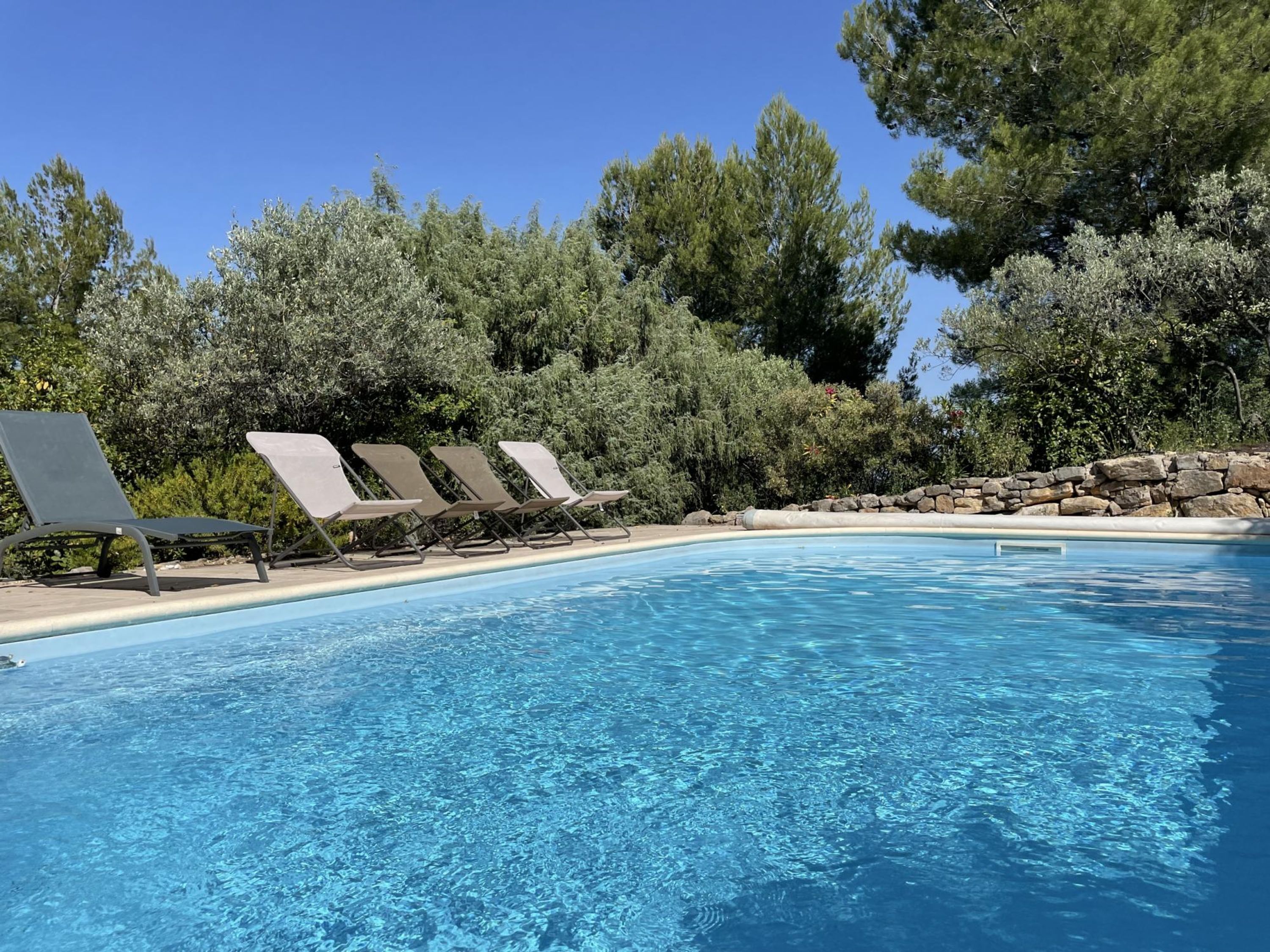 Una piscina azzurra con lettini e un muro in pietra.