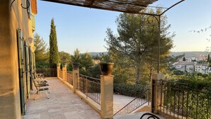 Une terrasse avec une table et des chaises, une pergola et une vue sur la ville et les arbres.