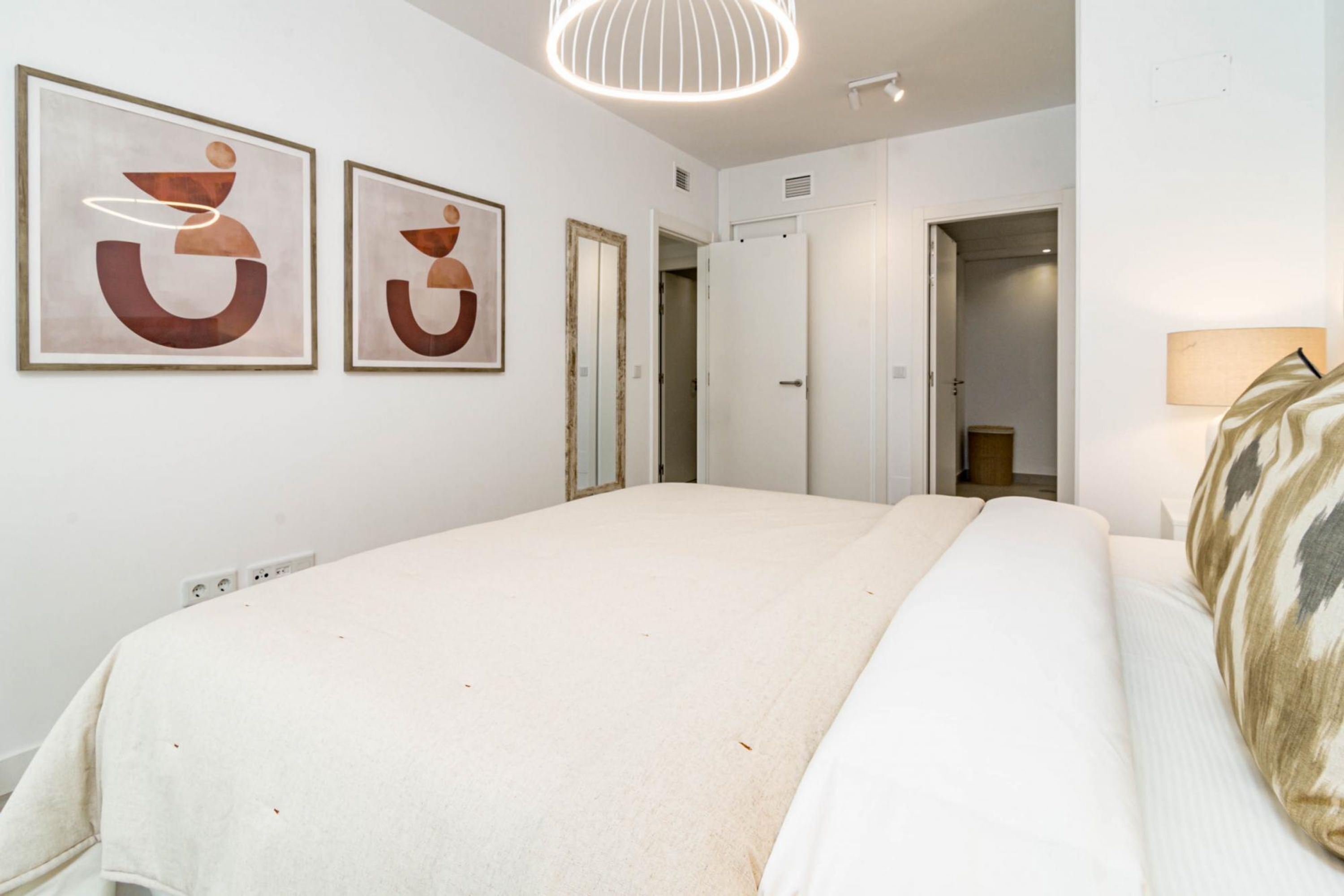 Ein Hotelzimmer mit einem großen Bett, einer Nachttischlampe und zwei gerahmten abstrakten Kunstwerken an der Wand.