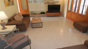 A living room with a sofa, a coffee table, a TV stand, and a lamp. - Villa Fig Tree Para 4 Personas (Calpe)