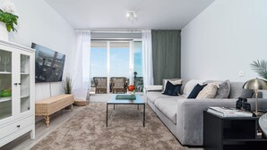 A modern living room with a sofa, a coffee table, and a TV on the wall. - OV2 1B - Bright and Modern 3 Bedroom Apartment (Estepona)