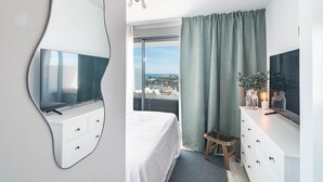 A modern hotel room with a large bed, a white dresser, a television, and a view of the city. - OV2 1B - Bright and Modern 3 Bedroom Apartment (Estepona)