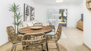 A modern living room with a round wooden dining table, wicker chairs, a sofa, and a large window with sheer curtains. - Ags48b- Great Location Close to Puerto Banus Casa (Marbella)