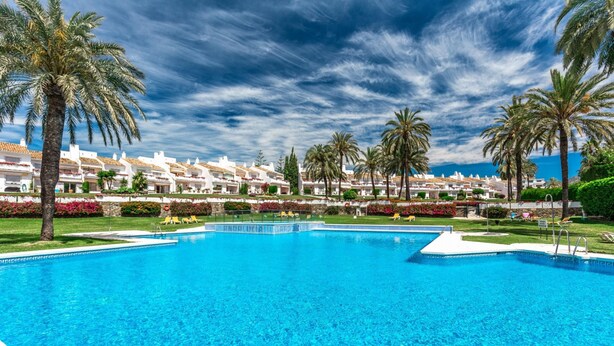 A large swimming pool surrounded by palm trees and a row of white buildings with red-tiled roofs. - Ags48b- Great Location Close to Puerto Banus Casa (Marbella)