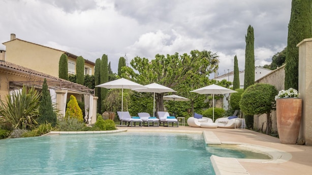 Area piscina con lettini e ombrelloni, immersa nel verde e con un edificio sullo sfondo.