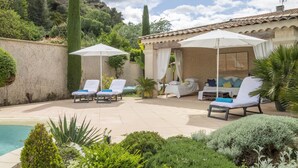 Zona piscina con lettini, ombrelloni e una chaise longue sotto una pergola.