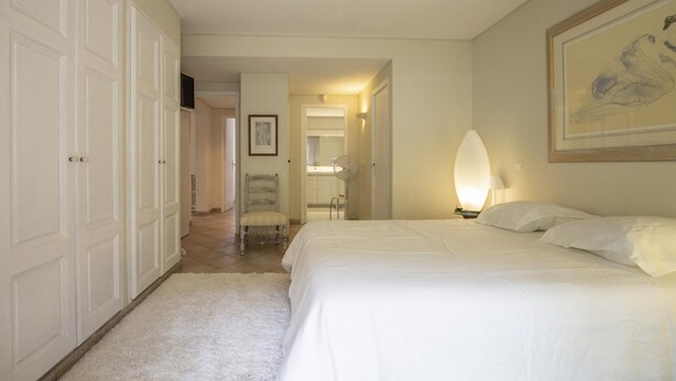 A bedroom with a large bed, a nightstand with a lamp, a framed artwork on the wall, and a door leading to another room. - Villa Ambre - Private Pool and Magnificent View (Digne-les-Bains)