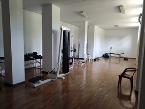 Un gimnasio con diversos equipos de ejercicio, suelo de madera y paredes blancas.