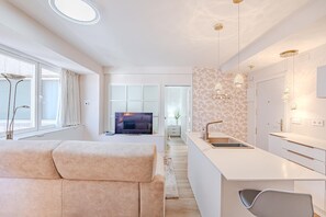 A modern living room with a sofa, a TV, and a kitchen area with a sink and cabinets. - Colon 904 in Madrid With 1 Bedrooms and 1 Bathrooms (Madrid)