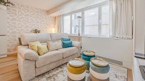 A living room with a beige sofa, decorative pillows, a floor lamp, and a large window with curtains.