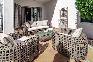 Een terras met rieten meubels, een tafel met glazen blad en een witte bank.