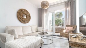 A modern living room with a beige sofa, a round coffee table, wicker furniture, and a large mirror on the wall. - SDG 2B - Holiday Home Senorio de Gonzaga (Marbella)
