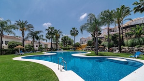 A swimming pool with a curved design, surrounded by palm trees and lounge chairs. - SDG 2B - Holiday Home Senorio de Gonzaga (Marbella)