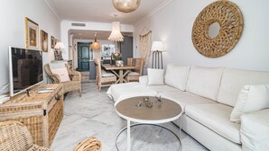 A modern living room with a white sofa, wicker furniture, a round coffee table, and a dining area with a wooden table and chairs. - SDG 2B - Holiday Home Senorio de Gonzaga (Marbella)