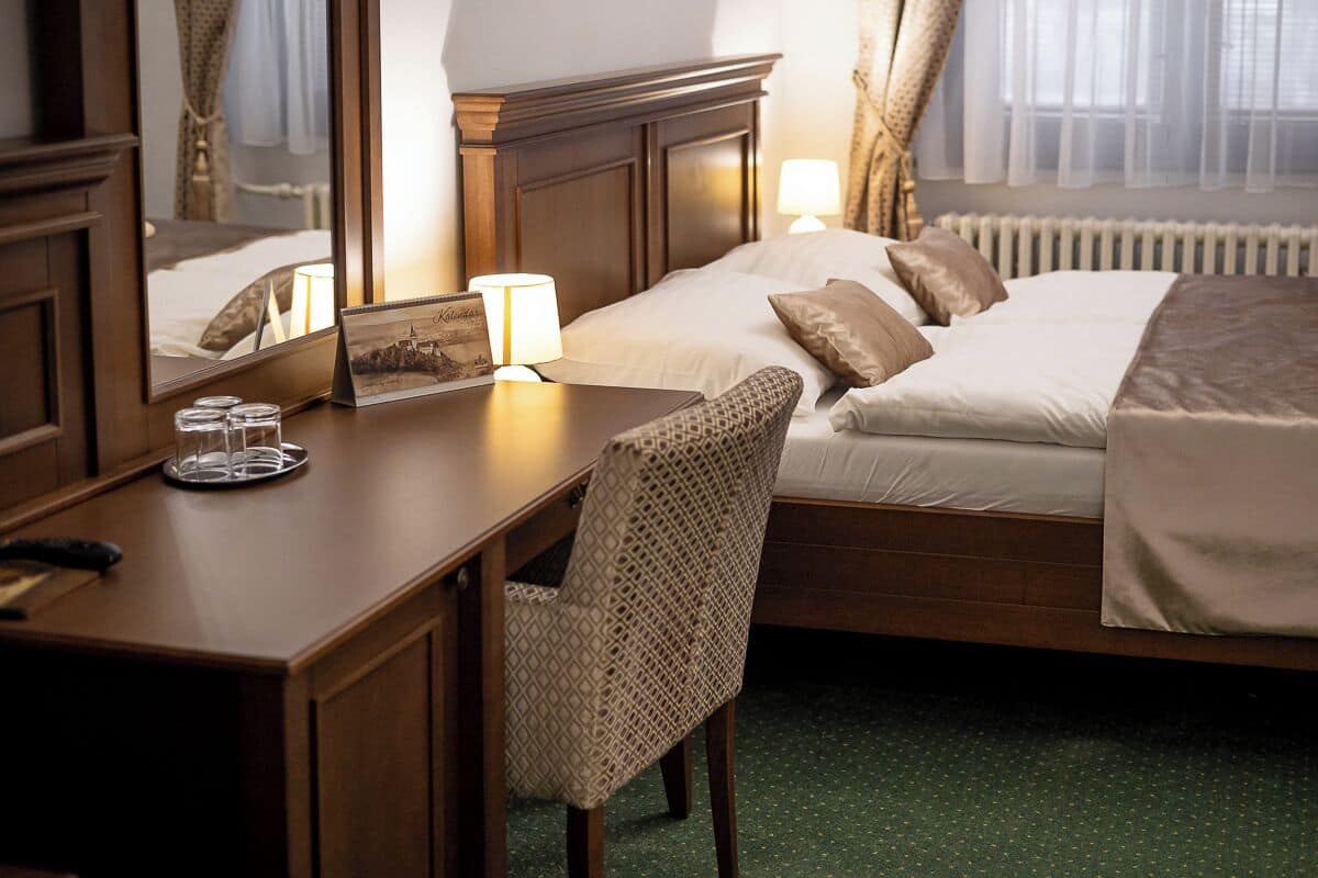 A hotel room with a bed, bedside table, chair, and a mirror.