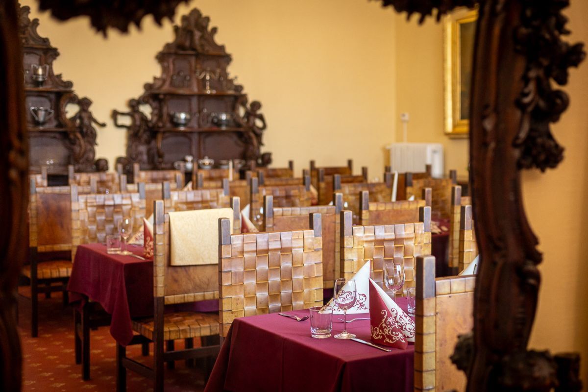Un comedor con sillas y mesas de madera, cada una con mantel rojo y servilleta blanca.