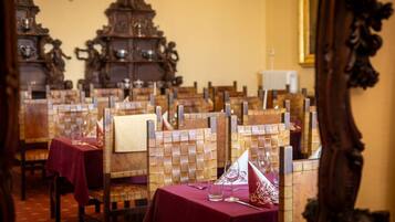 A dining area with wooden chairs and tables, each with a red tablecloth and a white napkin.