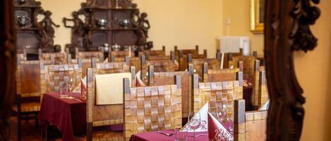 Un comedor con sillas y mesas de madera, cada una con mantel rojo y servilleta blanca.