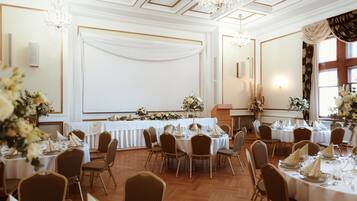 A banquet hall with round tables, chairs, chandeliers, and floral arrangements.
