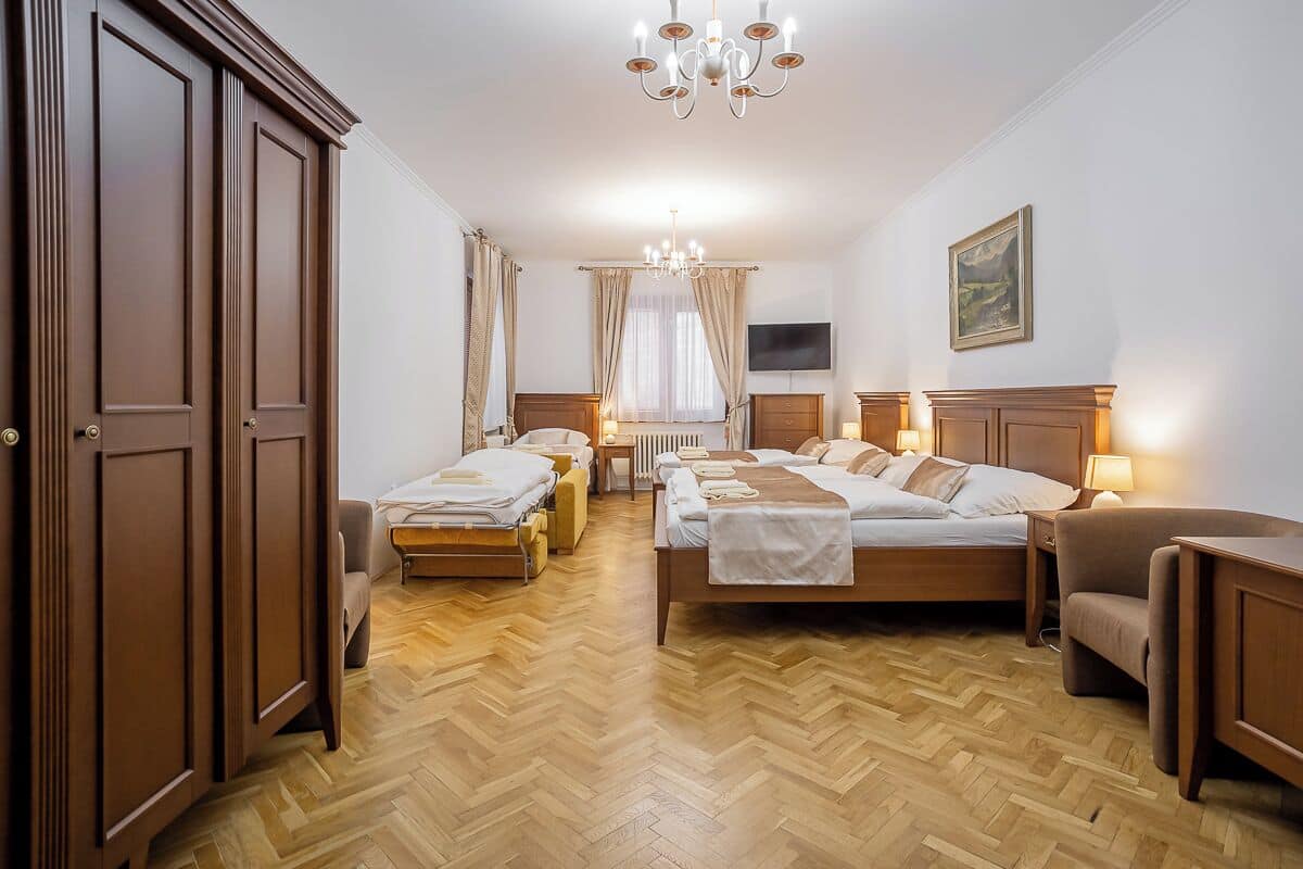 A hotel room with two beds, a TV, a painting, and a chandelier.