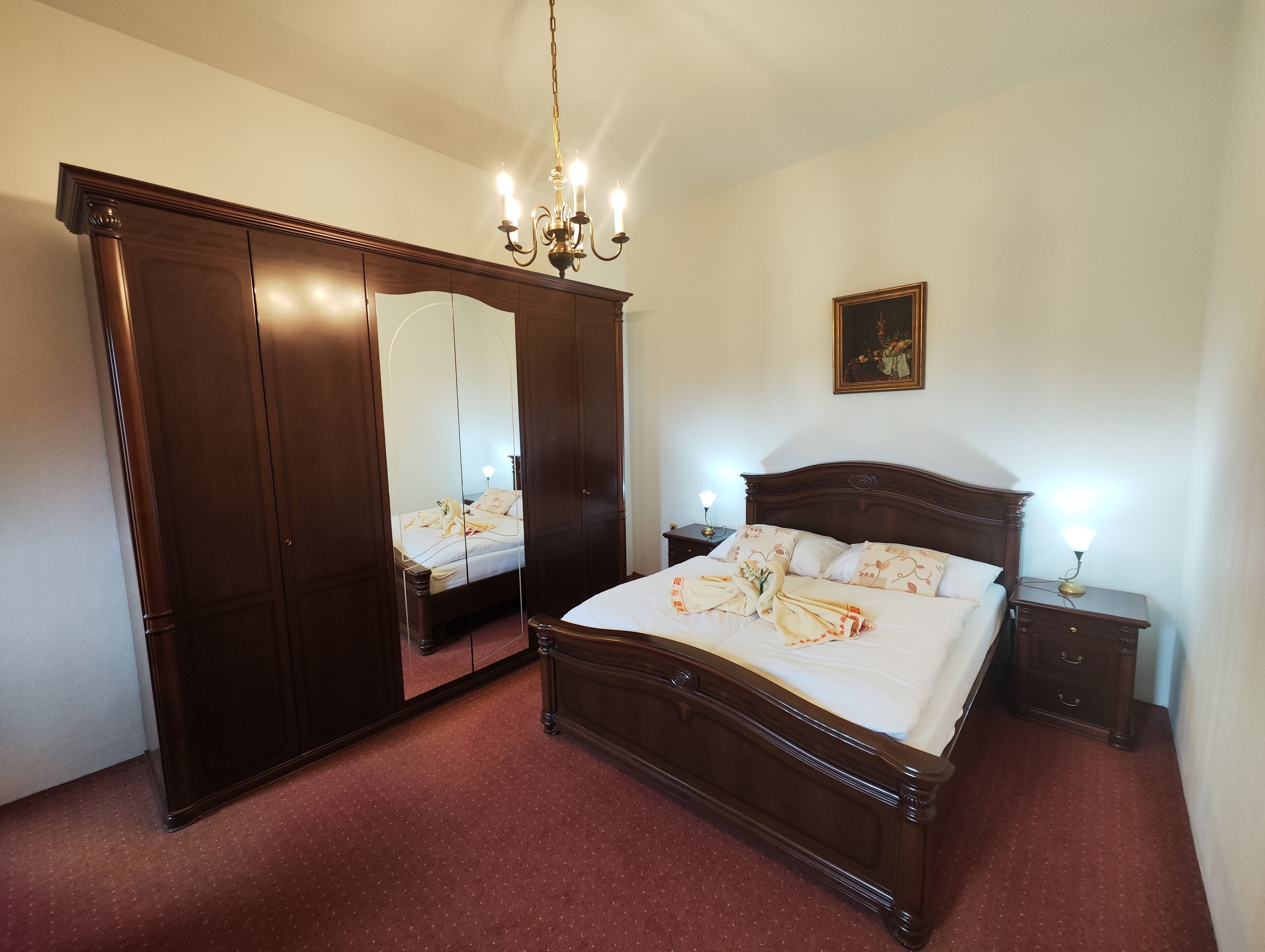 Een slaapkamer met een groot houten bed, een nachtkastje, een spiegel en een kroonluchter.