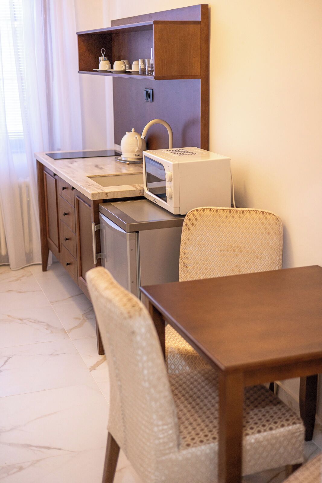 A compact kitchenette with a microwave, tea kettle, and a small shelf. There is a dining area with a wooden table and two wicker chairs.