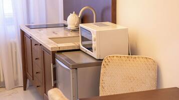 A compact kitchenette with a microwave, tea kettle, and a small shelf. There is a dining area with a wooden table and two wicker chairs.
