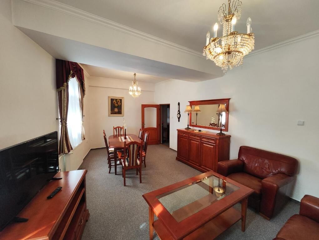 A living room with a TV, wooden furniture, a chandelier, and a dining area.