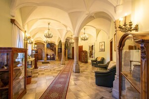 Um corredor imponente com pé direito alto, lustres e piso xadrez.