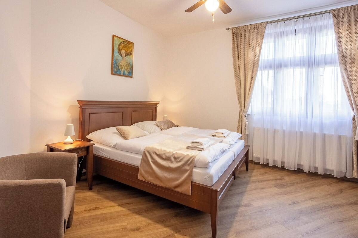 A bedroom with a wooden bed, a nightstand with a lamp, a chair, and a painting on the wall.