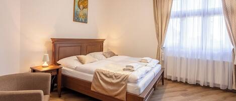 A bedroom with a wooden bed, a nightstand with a lamp, a chair, and a painting on the wall.