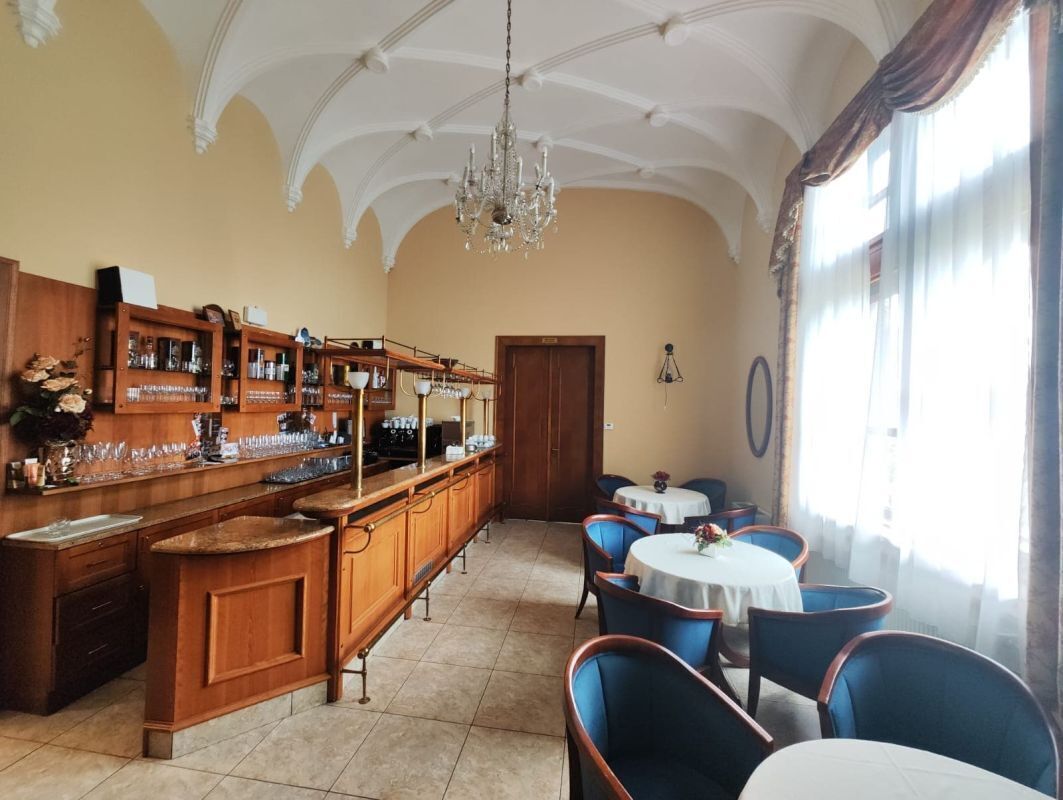 A bar area with wooden cabinets, a chandelier, and round tables with chairs.