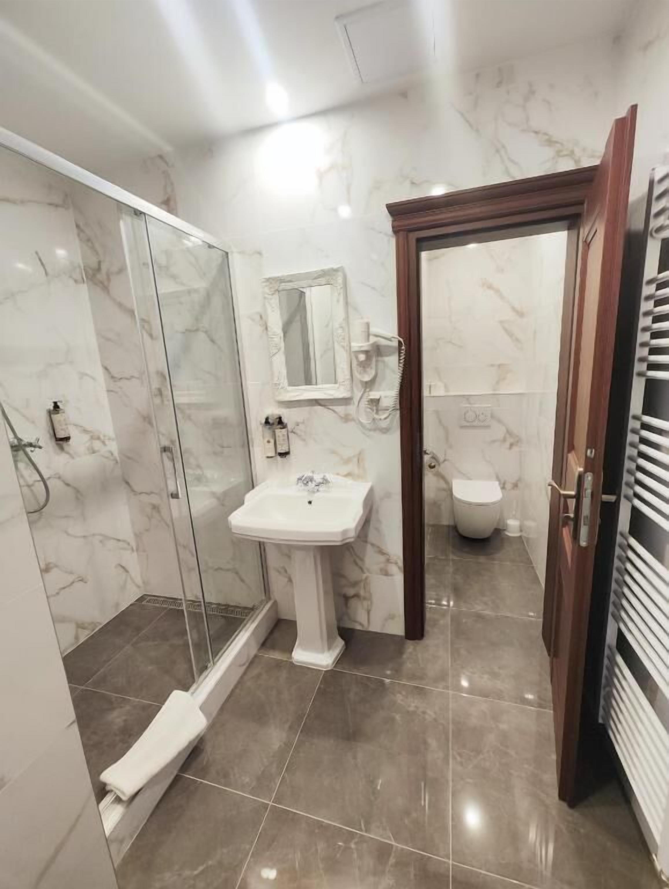 Un baño con cabina de ducha de vidrio, lavabo pedestal y inodoro.