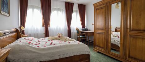 A hotel room with a large bed, wooden wardrobe, a desk with a chair, and a painting on the wall.
