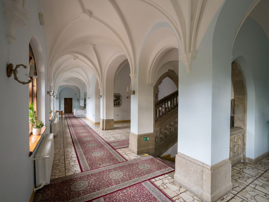 A corridor with arches, a red carpet, and a staircase.