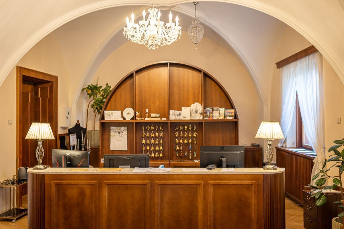 A reception desk with a chandelier, wooden paneling, and a plant.