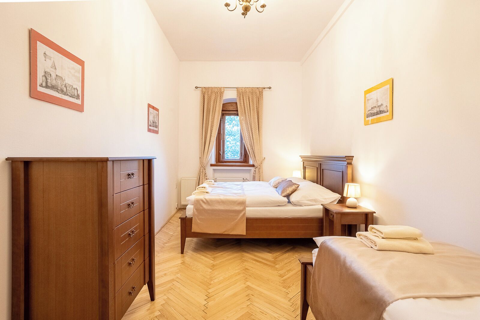 A bedroom with a wooden wardrobe, a bed with a headboard, a bedside table with a lamp, and a window with curtains.