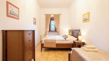 A bedroom with a wooden wardrobe, a bed with a headboard, a bedside table with a lamp, and a window with curtains.