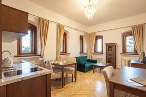 A room with a kitchen area, dining table, chairs, a green sofa, and a chandelier.