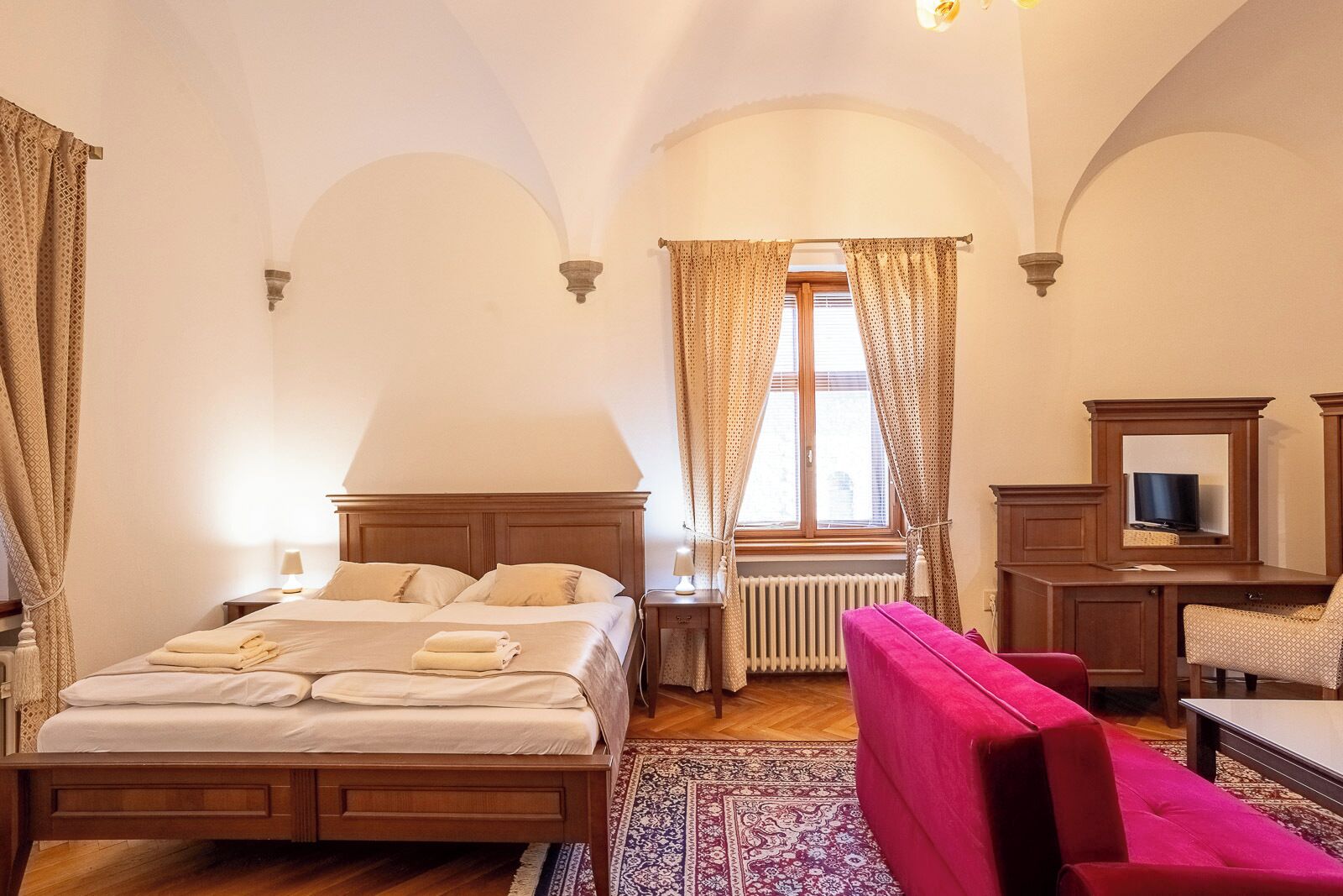 Ein Schlafzimmer mit einem Holzbett, einem roten Sessel, einem Fernseher und einem Fenster mit Vorhängen.