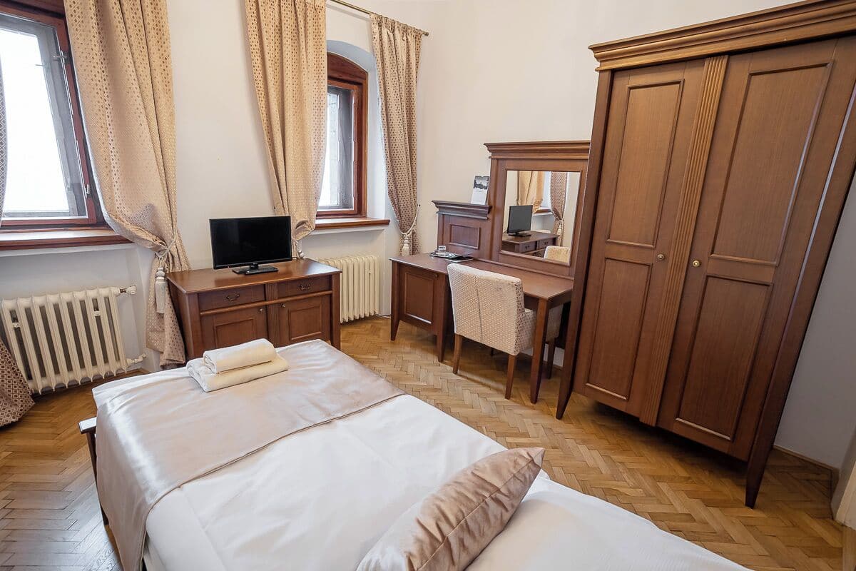 A hotel room with a bed, a desk with a computer, a television, and a wardrobe.