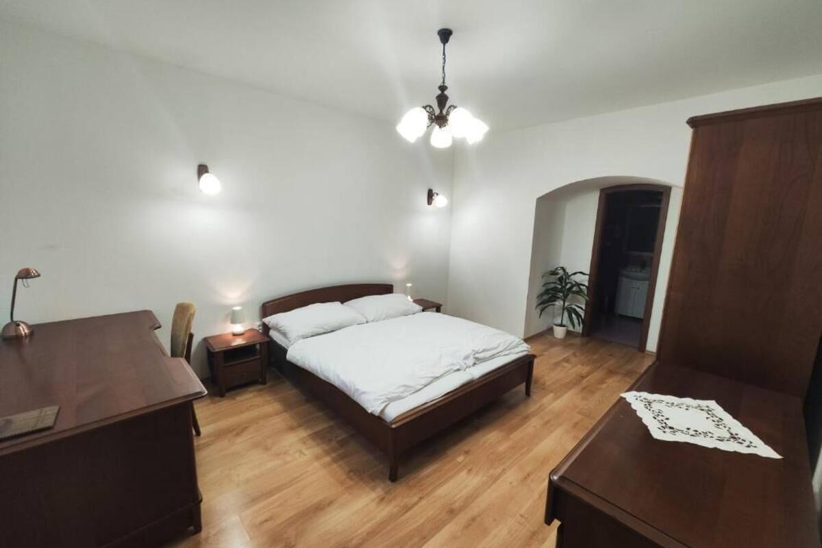 A bedroom with a wooden bed, bedside tables, a desk, and a ceiling light fixture.