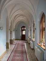 Corredor com tetos em arco, tapete vermelho e plantas em vasos nos parapeitos das janelas.