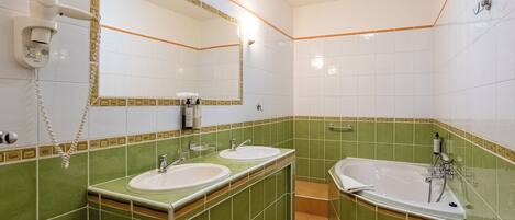 A bathroom with two sinks, a large bathtub, and a mirror with a telephone.