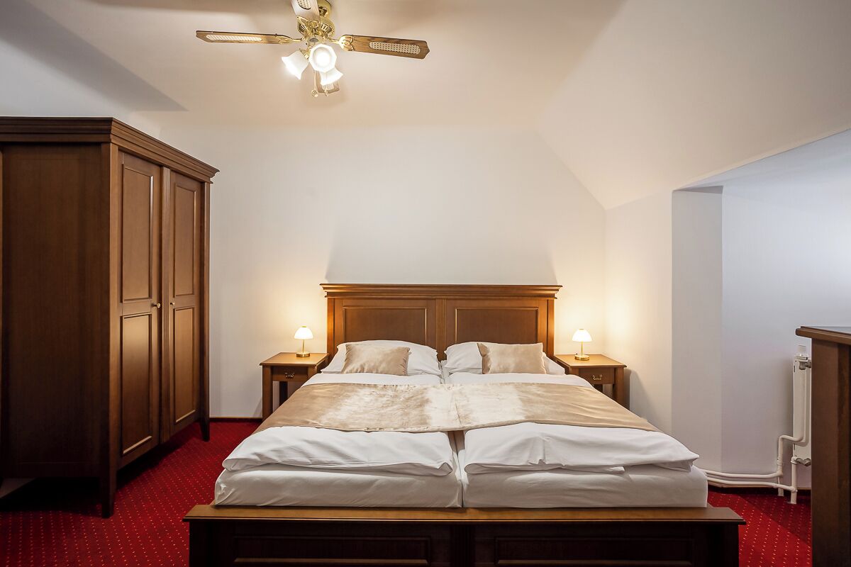 A bedroom with a wooden bed, two bedside tables with lamps, a ceiling fan, and a radiator.