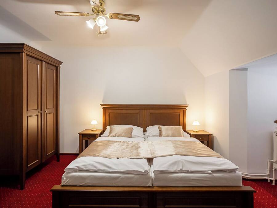 Un dormitorio con cama de madera, dos mesitas de noche con lámparas, un ventilador de techo y un radiador.